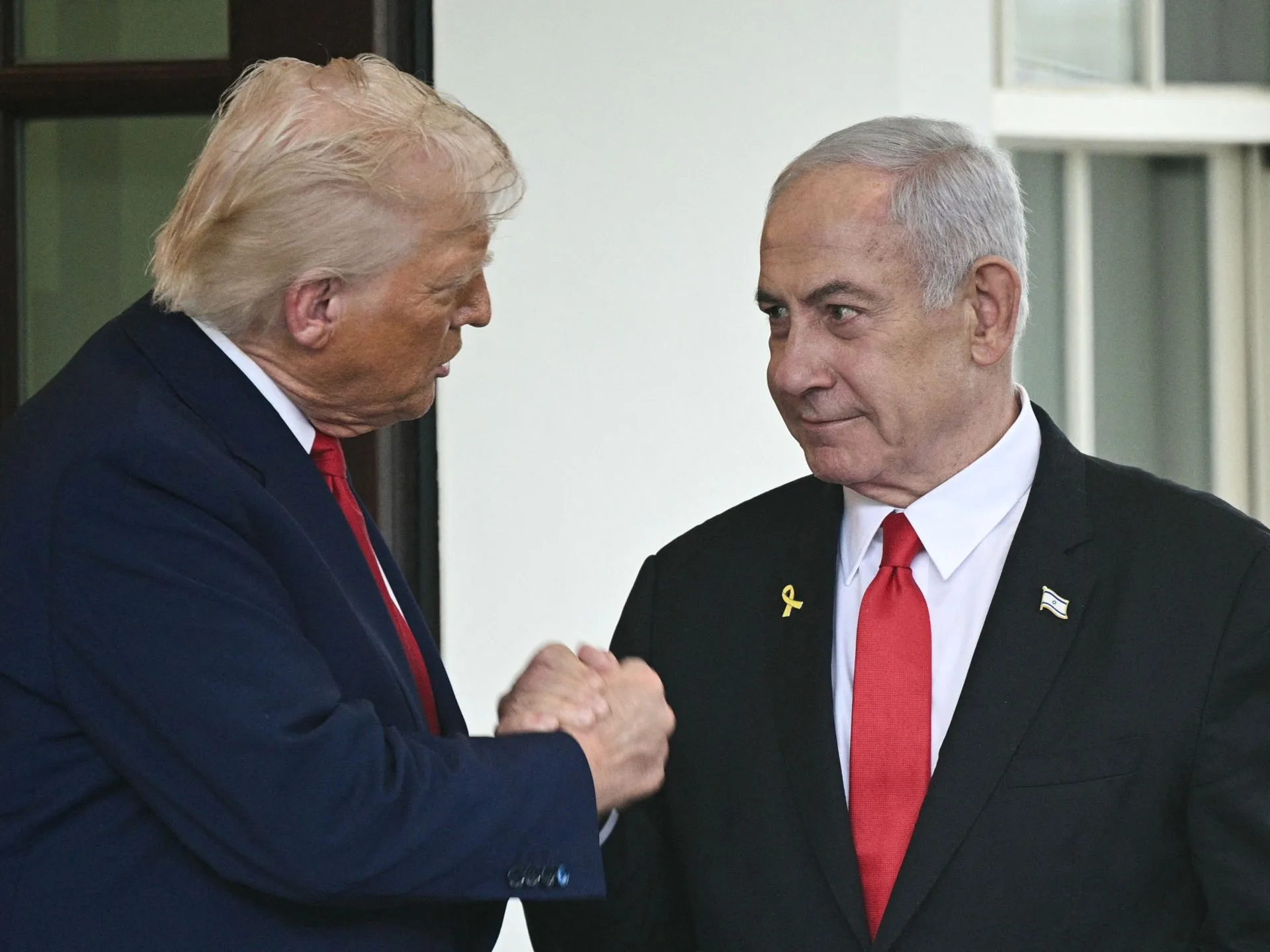 Donald Trump et Benjamin Netanyahu sont photographiés se serrant la main. Netanyahu porte sur sa veste une épingle représentant le drapeau israélien.