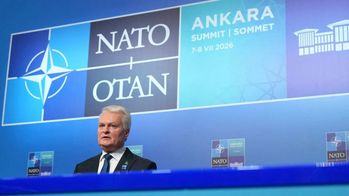 A man speaks at a media event in front of a backdrop bearing the NATO logo and an Ankara Summit announcement. The alliance name appears in English and French in the background.